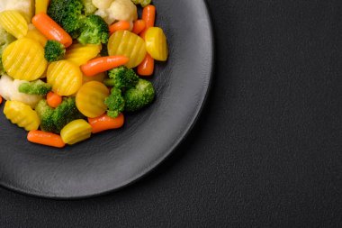 Delicious fresh vegetables steamed carrots, broccoli, cauliflower on a black plate on a dark concrete background