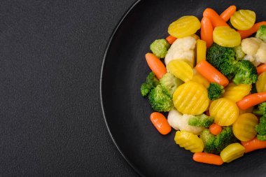 Delicious fresh vegetables steamed carrots, broccoli, cauliflower on a black plate on a dark concrete background