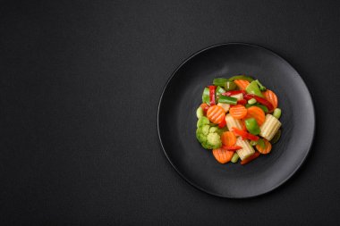 Delicious juicy broccoli vegetables, carrots, asparagus beans, bell peppers steamed in a black plate on a dark concrete background