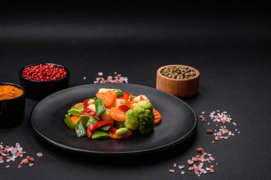 Delicious juicy broccoli vegetables, carrots, asparagus beans, bell peppers steamed in a black plate on a dark concrete background clipart