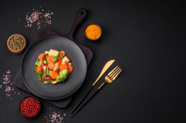 Delicious juicy broccoli vegetables, carrots, asparagus beans, bell peppers steamed in a black plate on a dark concrete background