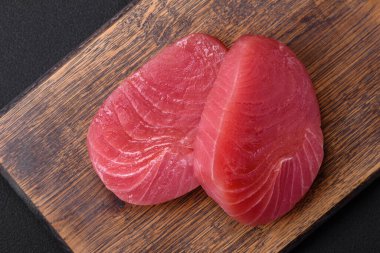 Two fresh slices of raw tuna fillet with spices and herbs on a dark concrete background