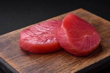 Two fresh slices of raw tuna fillet with spices and herbs on a dark concrete background