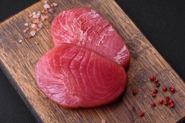 Two fresh slices of raw tuna fillet with spices and herbs on a dark concrete background