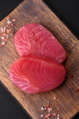 Two fresh slices of raw tuna fillet with spices and herbs on a dark concrete background