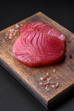 Two fresh slices of raw tuna fillet with spices and herbs on a dark concrete background