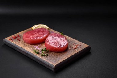 Two fresh slices of raw tuna fillet with spices and herbs on a dark concrete background