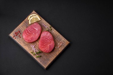 Two fresh slices of raw tuna fillet with spices and herbs on a dark concrete background