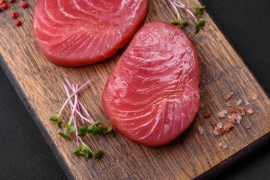 Two fresh slices of raw tuna fillet with spices and herbs on a dark concrete background