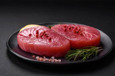 Two fresh slices of raw tuna fillet with spices and herbs on a dark concrete background