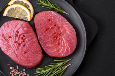 Two fresh slices of raw tuna fillet with spices and herbs on a dark concrete background