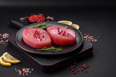 Two fresh slices of raw tuna fillet with spices and herbs on a dark concrete background