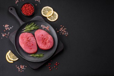 Two fresh slices of raw tuna fillet with spices and herbs on a dark concrete background