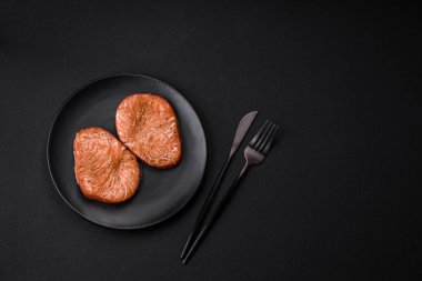 Two baked slices of tuna fillet with spices and herbs on a dark concrete background