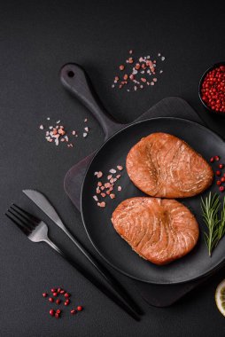 Two baked slices of tuna fillet with spices and herbs on a dark concrete background