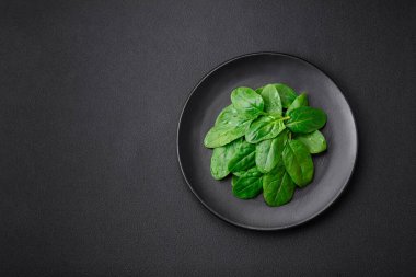 Fresh green spinach leaves on a black ceramic plate on a dark concrete background