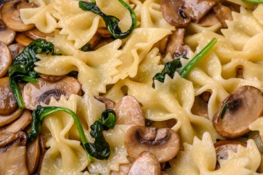 Delicious farfalle pasta with mushrooms, cheese and spinach with spices on a black plate on a dark concrete background