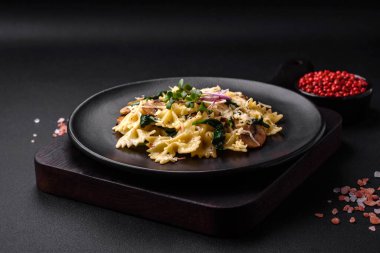 Delicious farfalle pasta with mushrooms, cheese and spinach with spices on a black plate on a dark concrete background