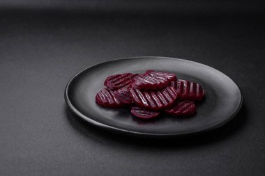 Delicious healthy boiled ruby-colored beets sliced on a black plate on a dark concrete background