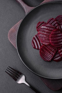 Delicious healthy boiled ruby-colored beets sliced on a black plate on a dark concrete background