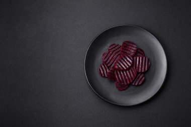 Delicious healthy boiled ruby-colored beets sliced on a black plate on a dark concrete background