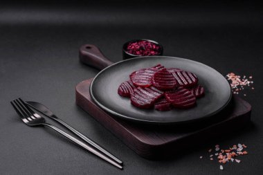 Delicious healthy boiled ruby-colored beets sliced on a black plate on a dark concrete background