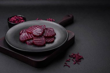 Delicious healthy boiled ruby-colored beets sliced on a black plate on a dark concrete background