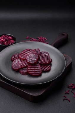 Delicious healthy boiled ruby-colored beets sliced on a black plate on a dark concrete background
