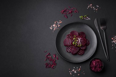 Delicious healthy boiled ruby-colored beets sliced on a black plate on a dark concrete background