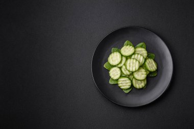 Delicious healthy raw cucumber sliced on a black ceramic plate on a dark concrete background