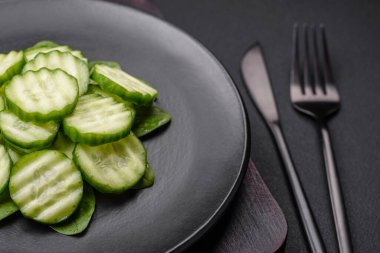 Delicious healthy raw cucumber sliced on a black ceramic plate on a dark concrete background