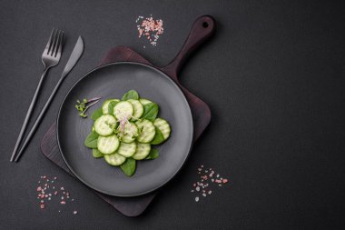 Delicious healthy raw cucumber sliced on a black ceramic plate on a dark concrete background