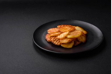 Delicious crispy fried potatoes in slices on a black ceramic plate on a dark concrete background