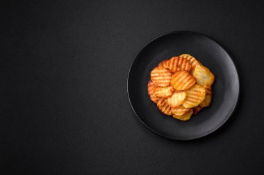 Delicious crispy fried potatoes in slices on a black ceramic plate on a dark concrete background