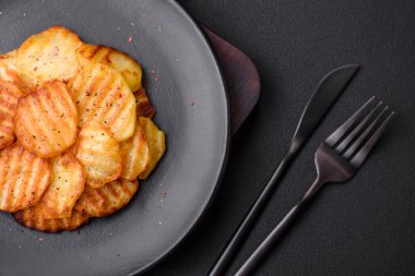 Delicious crispy fried potatoes in slices on a black ceramic plate on a dark concrete background