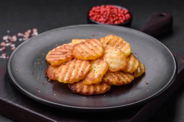 Delicious crispy fried potatoes in slices on a black ceramic plate on a dark concrete background