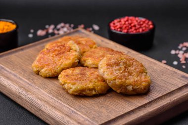 Delicious hearty vegetarian or vegan dish in the form of cutlets or patties consisting of potatoes, carrots, onions and beans on a dark concrete background