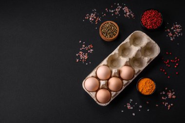 Fresh raw chicken eggs in beige color in a cardboard tray on a dark concrete background