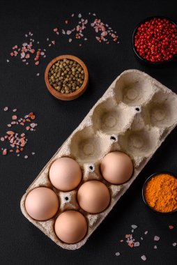 Fresh raw chicken eggs in beige color in a cardboard tray on a dark concrete background