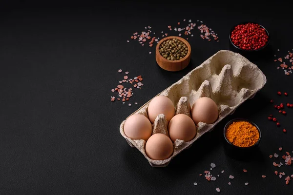 Fresh raw chicken eggs in beige color in a cardboard tray on a dark concrete background