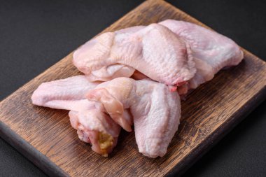 Raw chicken wings with salt, spices and herbs on a wooden cutting board on a dark concrete background