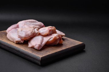 Raw chicken wings with salt, spices and herbs on a wooden cutting board on a dark concrete background