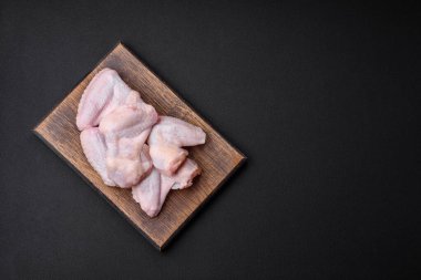 Raw chicken wings with salt, spices and herbs on a wooden cutting board on a dark concrete background