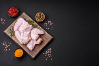 Raw chicken wings with salt, spices and herbs on a wooden cutting board on a dark concrete background