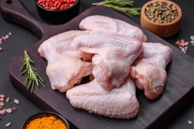 Raw chicken wings with salt, spices and herbs on a wooden cutting board on a dark concrete background