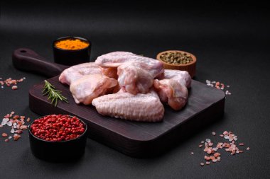 Raw chicken wings with salt, spices and herbs on a wooden cutting board on a dark concrete background