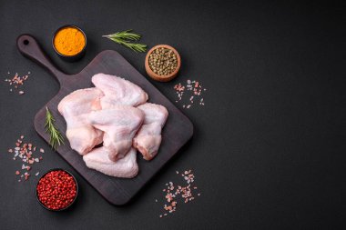 Raw chicken wings with salt, spices and herbs on a wooden cutting board on a dark concrete background