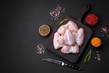 Raw chicken wings with salt, spices and herbs on a wooden cutting board on a dark concrete background