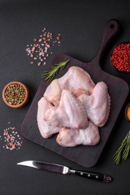 Raw chicken wings with salt, spices and herbs on a wooden cutting board on a dark concrete background