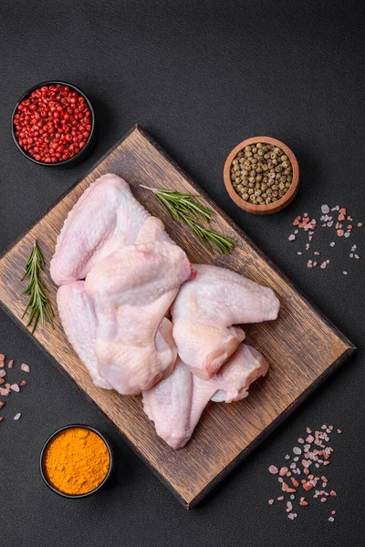 Raw chicken wings with salt, spices and herbs on a wooden cutting board on a dark concrete background